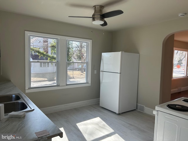 kitchen with arched walkways, white appliances, light wood-style floors, and baseboards