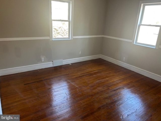 empty room featuring a wealth of natural light, dark wood-style flooring, visible vents, and baseboards