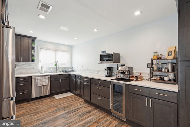 kitchen with beverage cooler, dark wood-type flooring, visible vents, appliances with stainless steel finishes, and backsplash