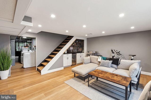 living area featuring wine cooler, light wood finished floors, a dry bar, washer / dryer, and stairs