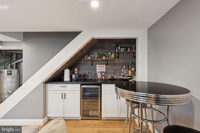 bar featuring light wood-type flooring, wine cooler, water heater, and a dry bar