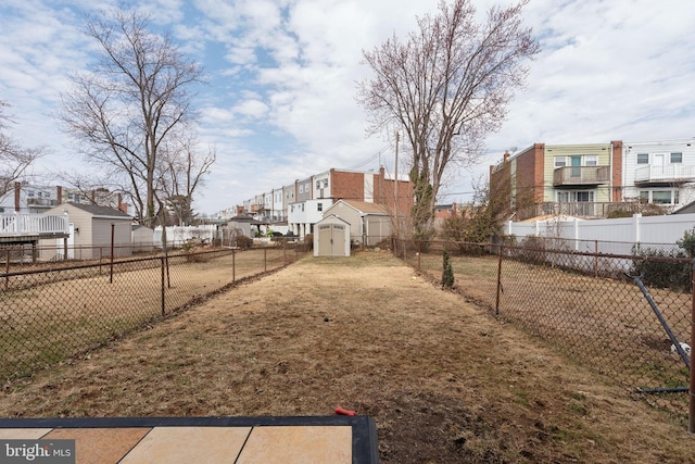 view of yard with a storage shed, a fenced backyard, a residential view, and an outbuilding