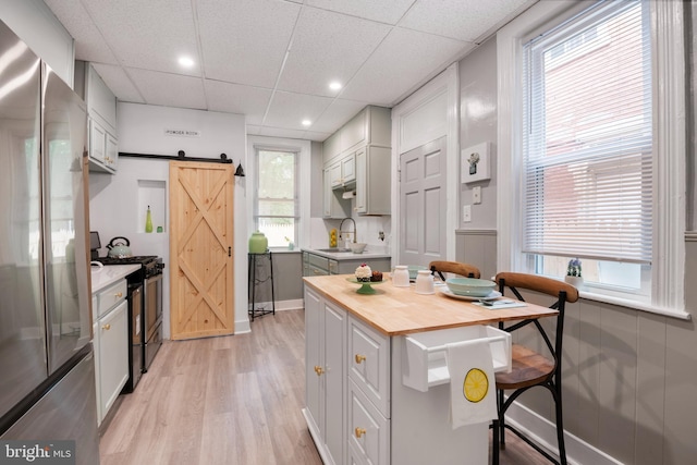 kitchen with a barn door, a breakfast bar area, a sink, wooden counters, and appliances with stainless steel finishes