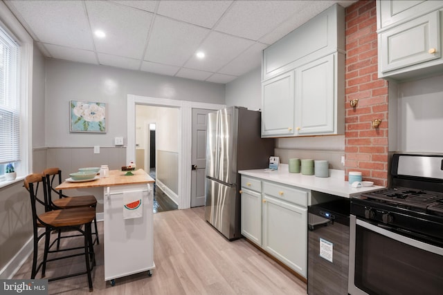 kitchen featuring a paneled ceiling, a breakfast bar, wooden counters, appliances with stainless steel finishes, and light wood-type flooring