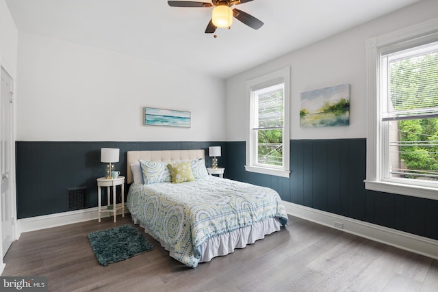 bedroom with a wainscoted wall, visible vents, ceiling fan, wood finished floors, and baseboards