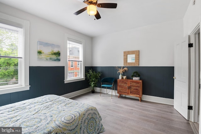 bedroom with a wainscoted wall, baseboards, a ceiling fan, and wood finished floors