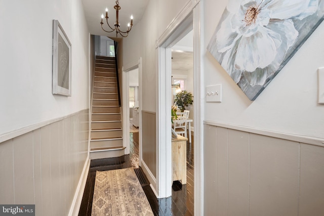 entryway with dark wood-style floors, a wainscoted wall, an inviting chandelier, and stairs