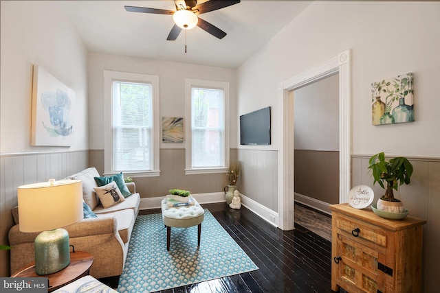 living area featuring dark wood-type flooring, wainscoting, and a ceiling fan