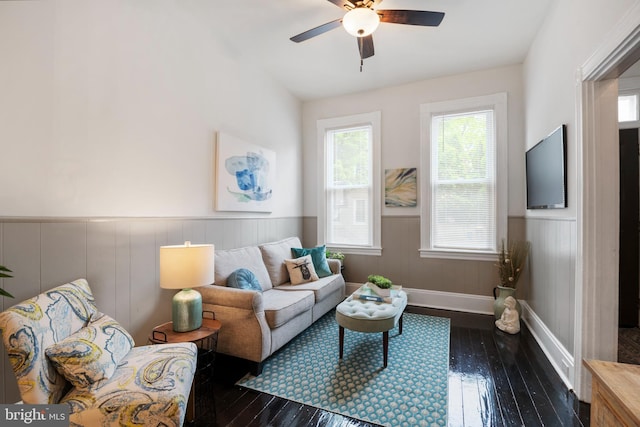 living area with a ceiling fan, wainscoting, and dark wood finished floors