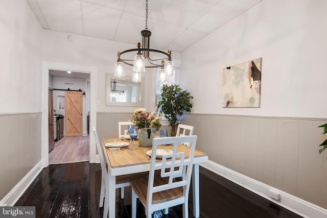 dining space with a barn door, a paneled ceiling, wood finished floors, wainscoting, and an inviting chandelier