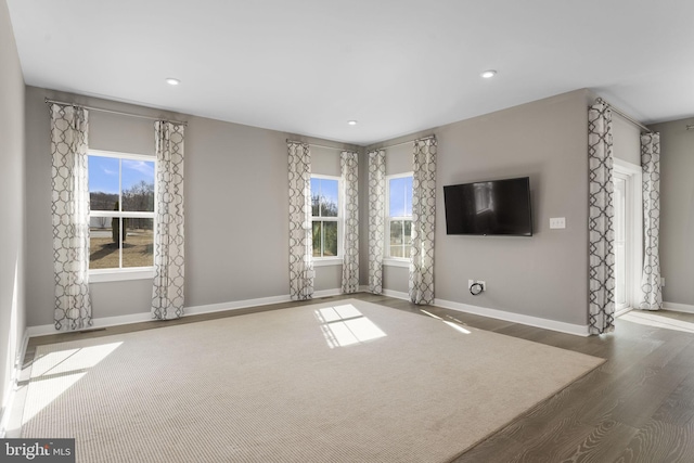 unfurnished living room featuring recessed lighting, plenty of natural light, baseboards, and wood finished floors