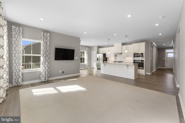 unfurnished living room featuring baseboards, wood finished floors, a sink, and recessed lighting