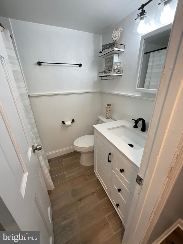 full bathroom with wood tiled floor, a wainscoted wall, vanity, and toilet