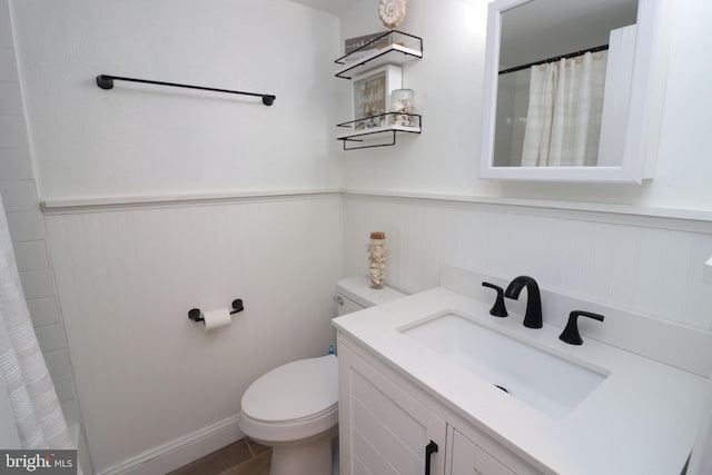 full bathroom featuring a wainscoted wall, curtained shower, vanity, and toilet