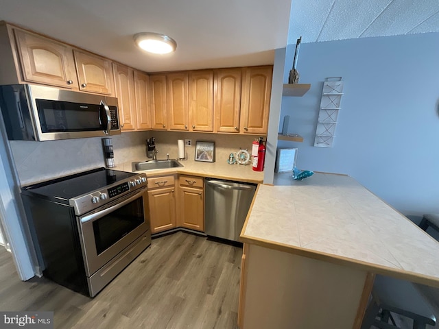 kitchen with light wood finished floors, light brown cabinetry, appliances with stainless steel finishes, a sink, and a peninsula