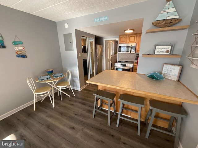 kitchen with electric panel, dark wood-style flooring, a peninsula, stainless steel appliances, and a kitchen bar