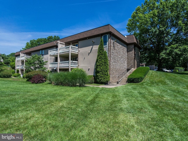 back of property with brick siding, a lawn, and a balcony