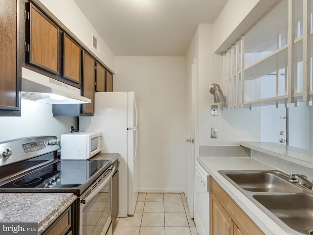 kitchen featuring light tile patterned floors, under cabinet range hood, white appliances, a sink, and brown cabinets