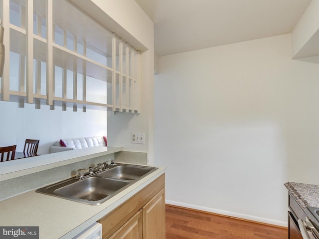 kitchen with white dishwasher, light brown cabinets, wood finished floors, a sink, and baseboards