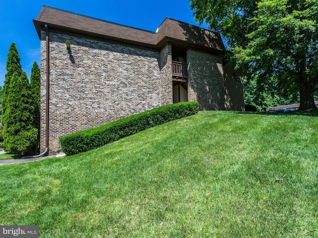 view of property exterior featuring a yard, brick siding, and a balcony