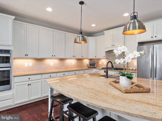 kitchen featuring a breakfast bar, dark wood-style flooring, white cabinetry, appliances with stainless steel finishes, and tasteful backsplash