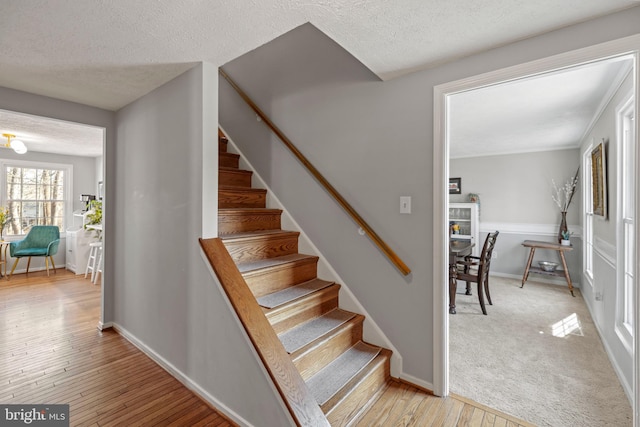 stairs with carpet, a textured ceiling, wood finished floors, a lit fireplace, and baseboards