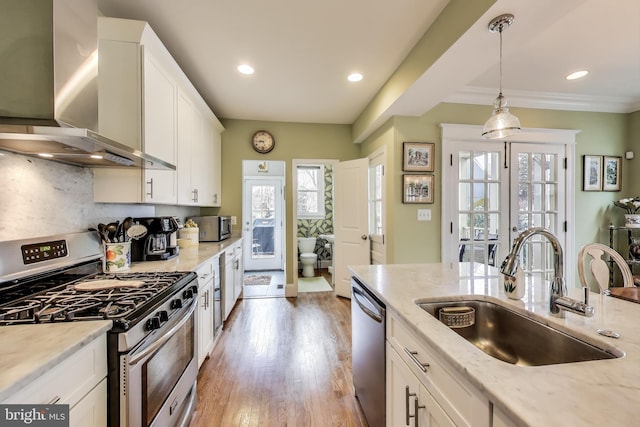 kitchen with white cabinetry, stainless steel appliances, wall chimney range hood, and a sink