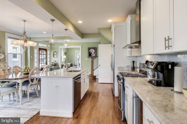 kitchen featuring wood finished floors, a sink, appliances with stainless steel finishes, white cabinetry, and wall chimney exhaust hood