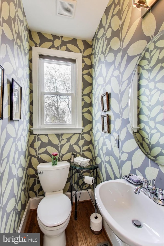 half bath featuring a sink, visible vents, toilet, and wallpapered walls