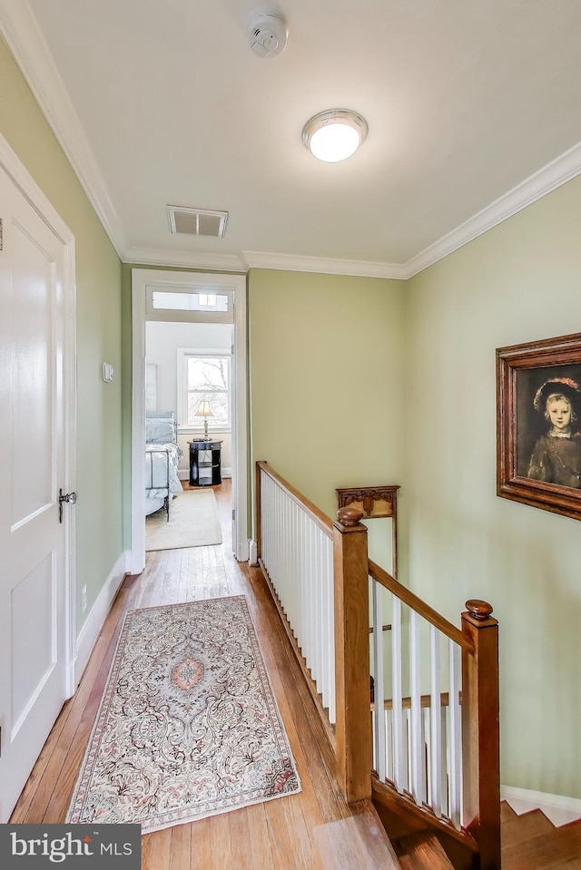 corridor featuring visible vents, an upstairs landing, ornamental molding, hardwood / wood-style floors, and baseboards