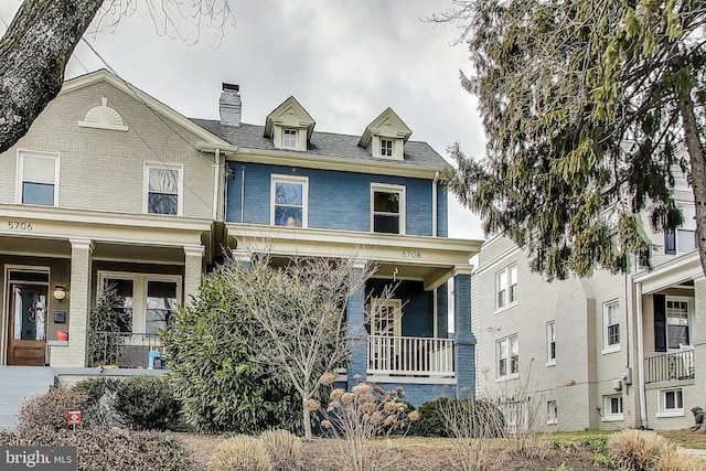 view of front facade featuring brick siding, a porch, and a chimney