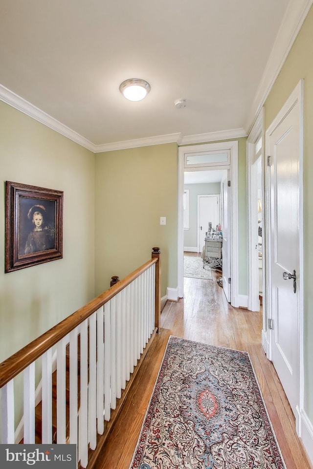 hall with light wood-style flooring, an upstairs landing, baseboards, and ornamental molding