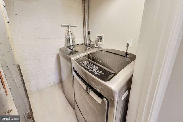 laundry area with laundry area, light tile patterned floors, independent washer and dryer, and brick wall