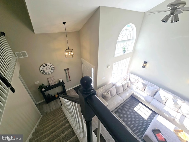 living room featuring ceiling fan with notable chandelier, a high ceiling, visible vents, baseboards, and stairs