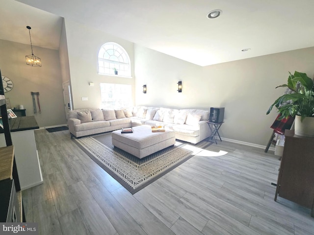 living area with a notable chandelier, wood finished floors, a towering ceiling, and baseboards