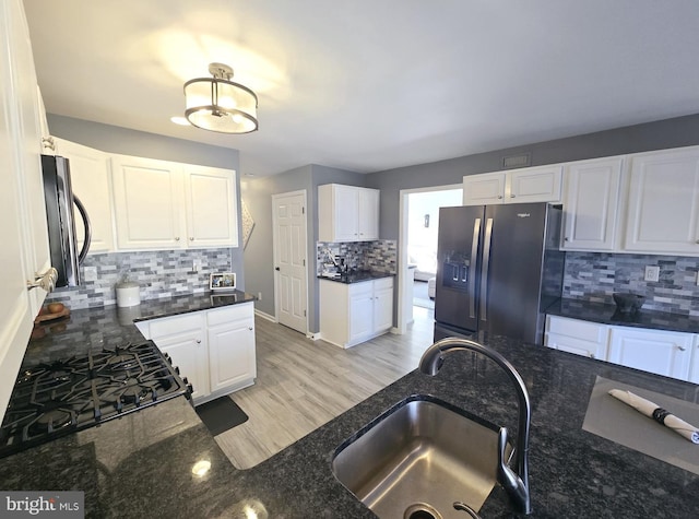 kitchen with tasteful backsplash, dark stone counters, white cabinets, fridge with ice dispenser, and a sink