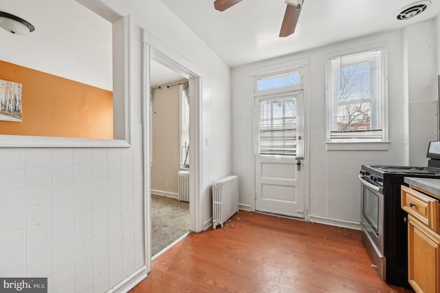 doorway featuring radiator heating unit, wood finished floors, visible vents, and tile walls