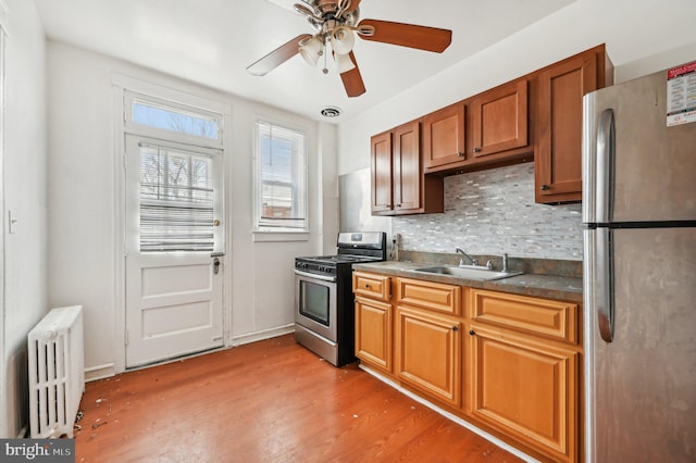 kitchen with a sink, appliances with stainless steel finishes, radiator, light wood finished floors, and tasteful backsplash