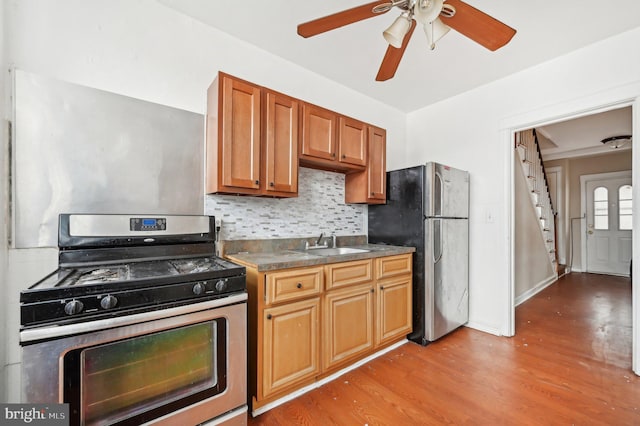 kitchen featuring light wood finished floors, decorative backsplash, dark countertops, appliances with stainless steel finishes, and a sink