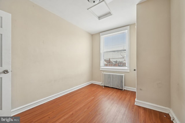 spare room with radiator, attic access, baseboards, and wood finished floors