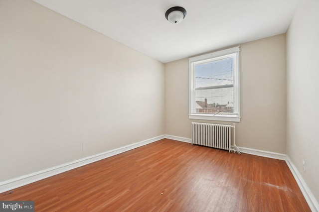 empty room with radiator heating unit, baseboards, and wood finished floors