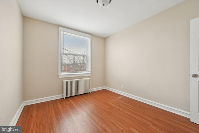 spare room with radiator, baseboards, and wood finished floors