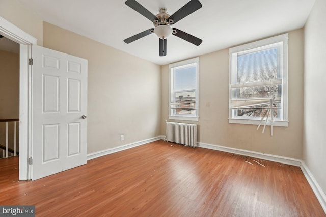 unfurnished bedroom with radiator, ceiling fan, baseboards, and wood finished floors