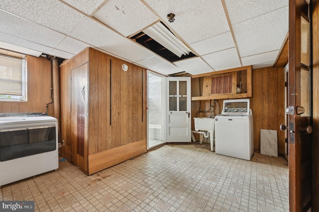 laundry room with laundry area, wooden walls, independent washer and dryer, light floors, and a sink