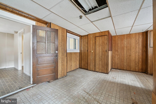 unfurnished room with light floors, a drop ceiling, and wooden walls