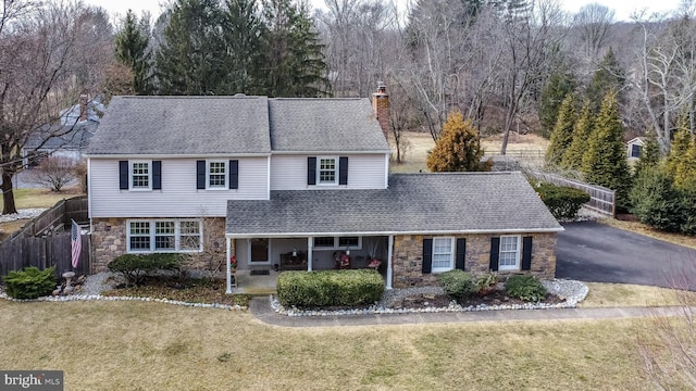 traditional home with a patio, stone siding, a chimney, aphalt driveway, and a front lawn