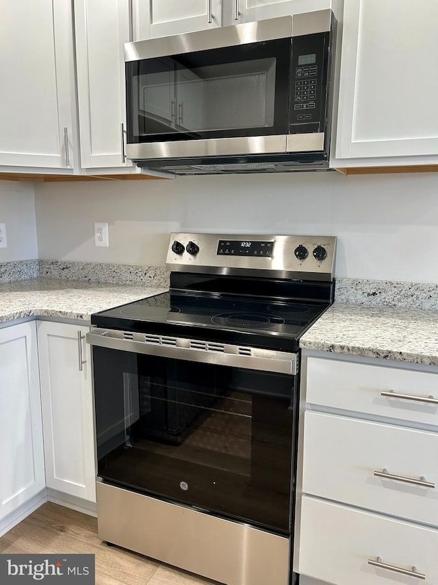 kitchen featuring appliances with stainless steel finishes, light wood-style floors, light stone countertops, and white cabinets