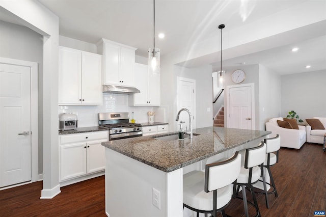 kitchen featuring stainless steel gas range oven, a center island with sink, dark stone counters, under cabinet range hood, and a sink