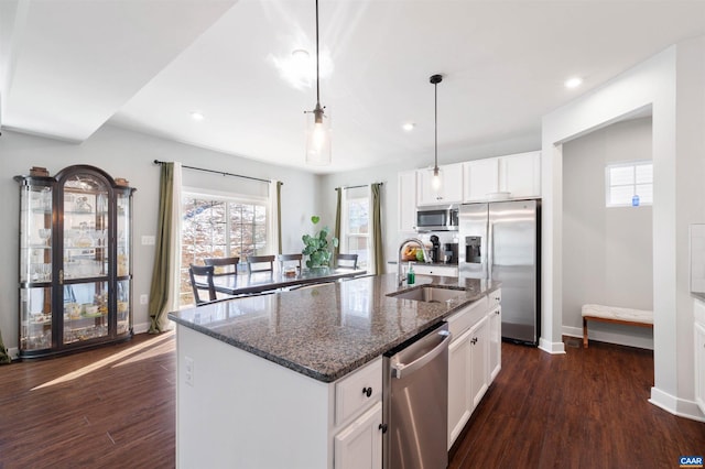 kitchen featuring stainless steel appliances, white cabinets, a kitchen island with sink, a sink, and dark stone countertops