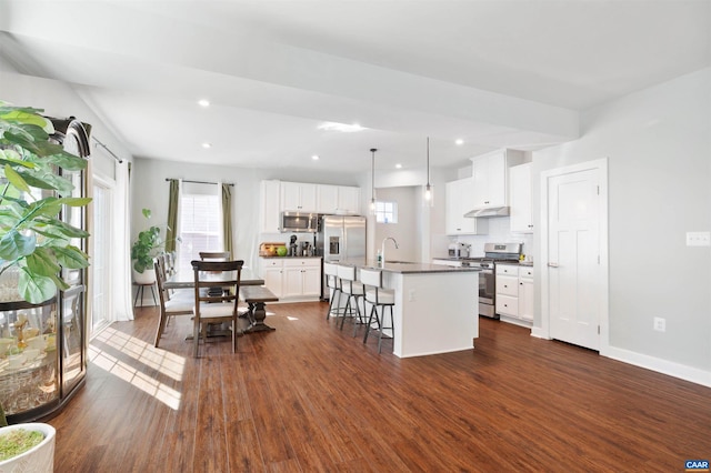 kitchen with a breakfast bar, pendant lighting, a center island with sink, appliances with stainless steel finishes, and white cabinets